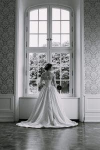 Eine Braut in einem Hochzeitskleid schaut aus einem Fenster.