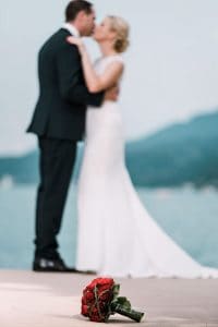 Eine Braut und ein Bräutigam küssen sich vor einem See.