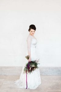 Eine Braut in einem weißen Kleid mit einem lila Blumenstrauß.