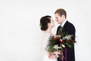 Eine Braut und ein Bräutigam küssen sich vor einer weißen Wand.