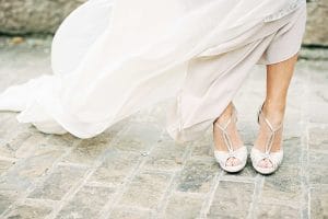 Eine Braut in einem weißen Kleid steht auf einer Kopfsteinpflasterstraße.