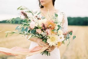 Eine Braut hält einen Blumenstrauß auf einem Feld.