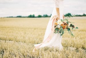 Eine Braut hält einen Blumenstrauß auf einem Feld.
