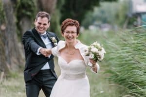 Eine Braut und ein Bräutigam laufen durch ein Feld.