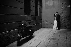 Ein Schwarz-Weiß-Foto einer Braut und eines Bräutigams, die sich vor einem Roller küssen.