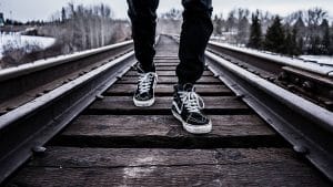 Die Füße einer Person, die auf einem Bahngleis steht.