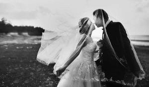 Schwarz-Weiß-Foto einer Braut und eines Bräutigams, die sich am Strand küssen.