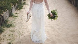 Eine Braut geht in einem weißen Hochzeitskleid den Strand entlang.