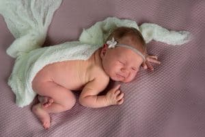 Ein neugeborenes Mädchen, in eine weiße Decke gehüllt, liegt auf einer rosa Decke.