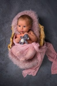 Ein neugeborenes Baby in einem rosa Korb mit einem Teddybären.