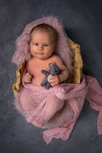 Ein neugeborenes Baby, eingewickelt in eine rosa Decke, mit einem Teddybären.