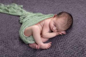 Ein neugeborenes Baby, das in einem grünen Tragetuch schläft.