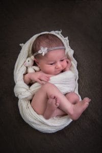 Ein Neugeborenes, eingewickelt in eine weiße Decke, mit einem Teddybären.