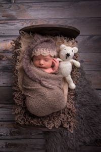 Ein neugeborenes Baby, eingewickelt in eine Decke mit einem Teddybären.