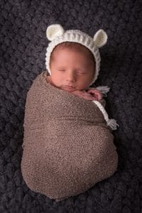 Ein Neugeborenes, eingehüllt in eine gestrickte Bärenmütze.