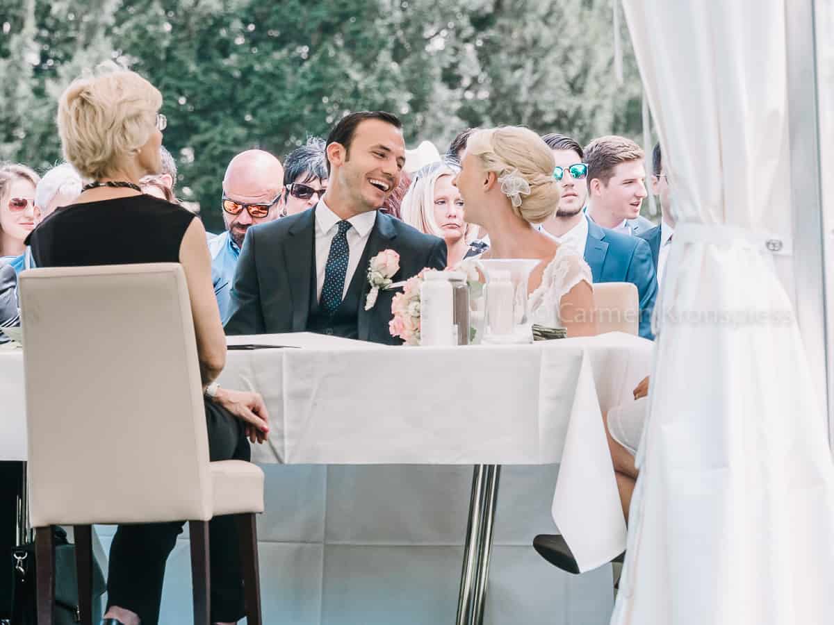 Eine Braut und ein Bräutigam sitzen an einem Tisch vor einer Menschenmenge.