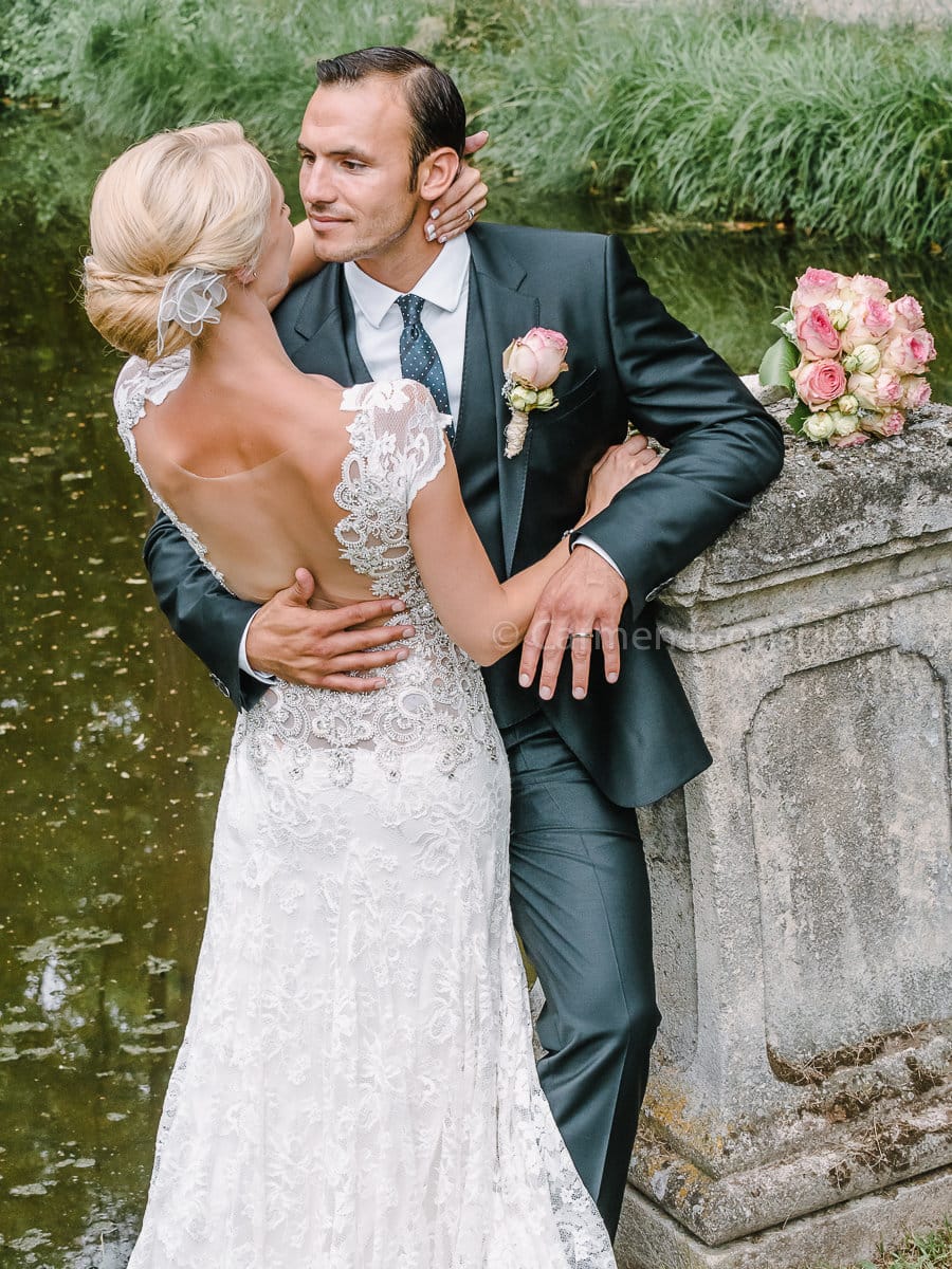 Eine Braut und ein Bräutigam küssen sich vor einem Teich.