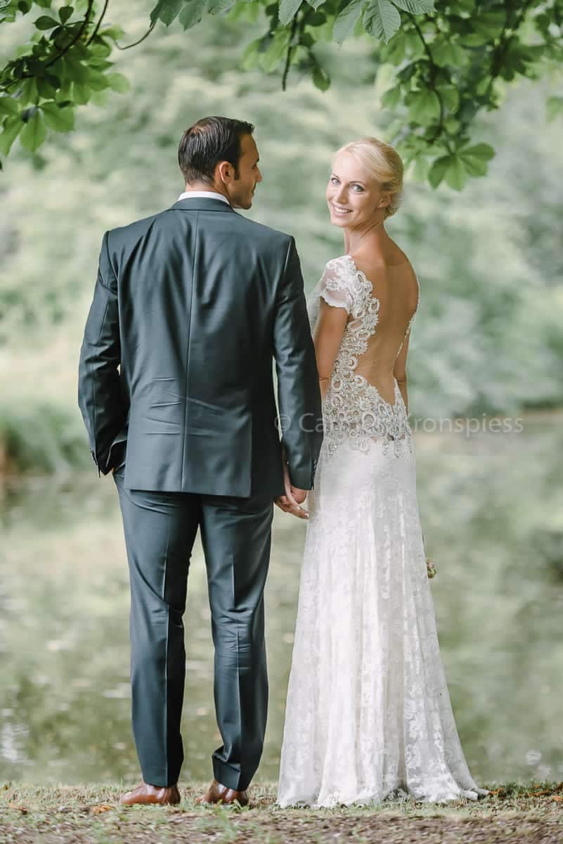 Eine Braut und ein Bräutigam stehen neben einem Teich.