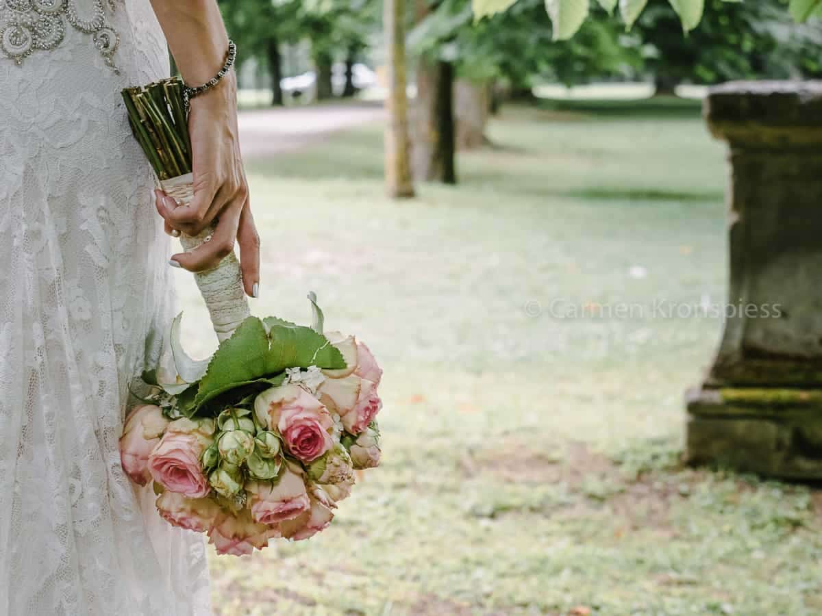Eine Braut hält einen Strauß rosa Rosen in einem Park.