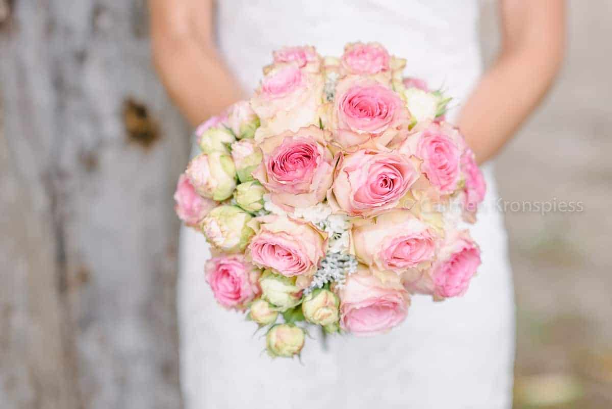 Eine Braut hält einen Strauß rosa Rosen.