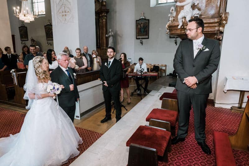 Eine Braut und ein Bräutigam gehen in einer Kirche den Altar entlang.
