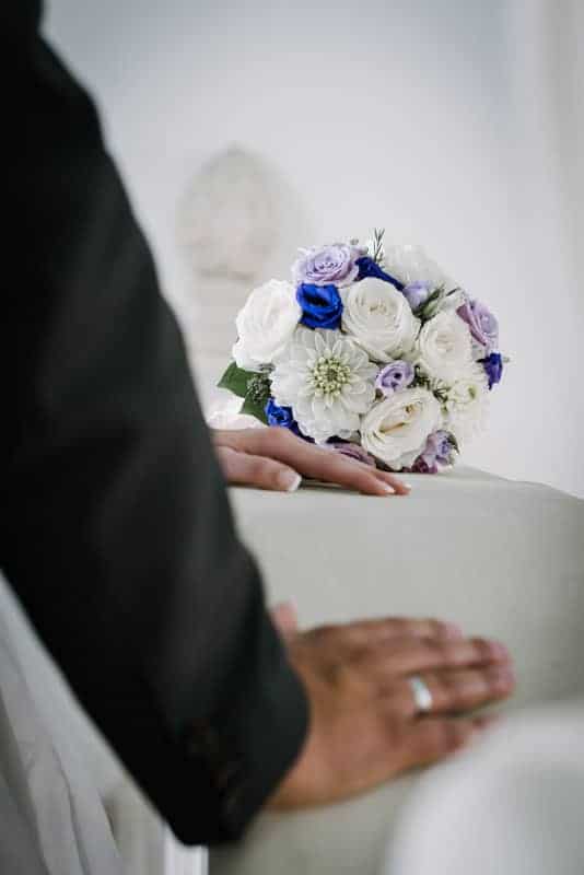 Eine Braut und ein Bräutigam halten einen Strauß weißer und blauer Blumen.
