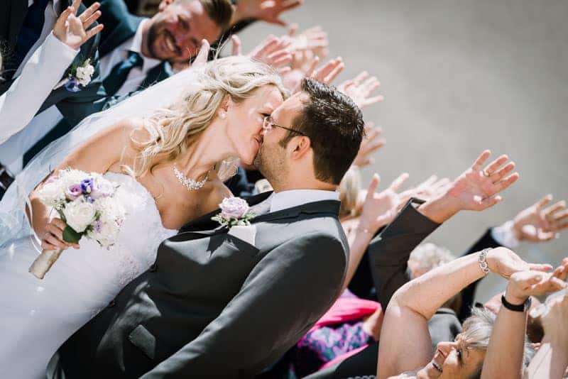 Eine Braut und ein Bräutigam küssen sich vor den Augen ihrer Hochzeitsgäste.