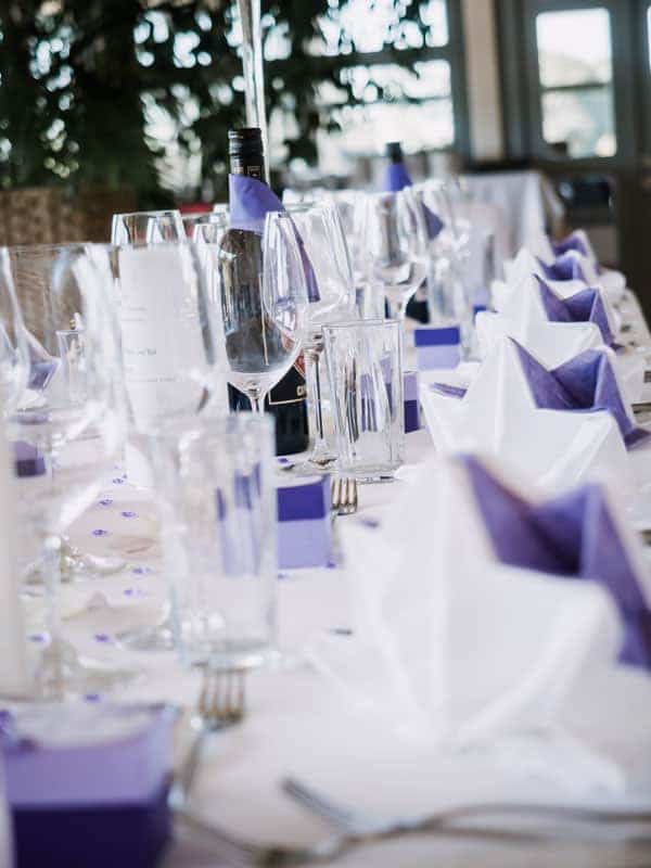 Ein Tisch, der mit lila und weißen Servietten und Gläsern gedeckt ist.