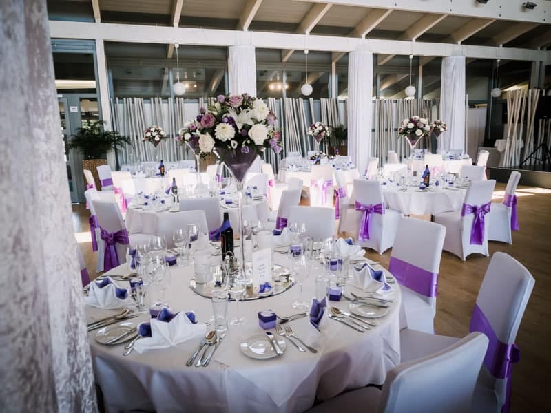 Ein Hochzeitsempfang mit lila-weißen Tischen und Stühlen.