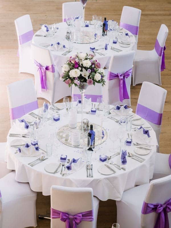 Ein runder Tisch mit lila-weißen Stühlen und Schärpen.