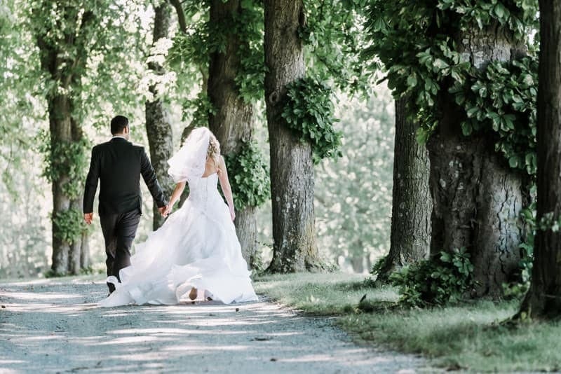 Eine Braut und ein Bräutigam gehen einen Pfad in einem Waldgebiet entlang.