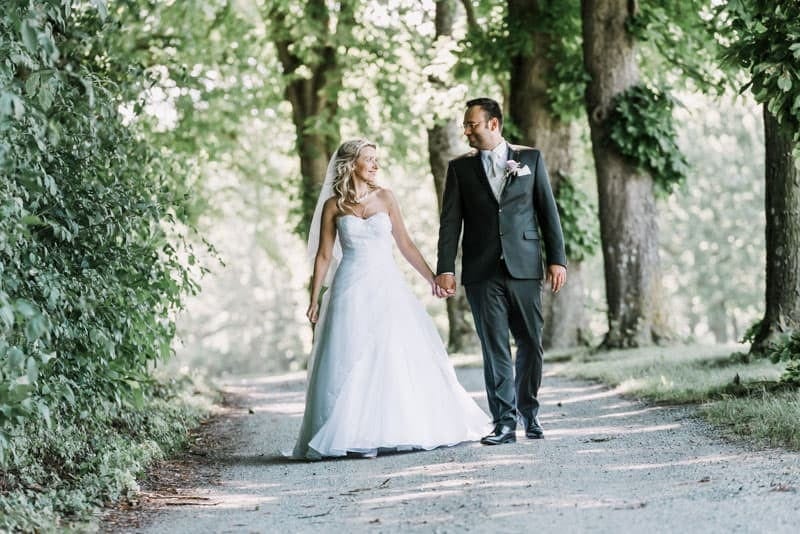 Eine Braut und ein Bräutigam gehen einen Pfad im Wald entlang.