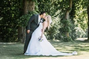 Eine Braut und ein Bräutigam küssen sich in einem Park.