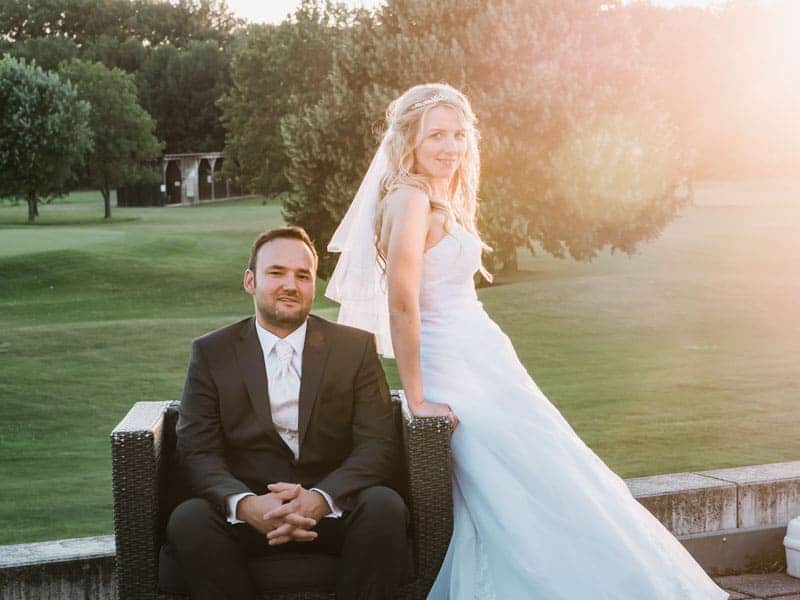 Ein Brautpaar sitzt auf einem Stuhl vor einem Golfplatz.