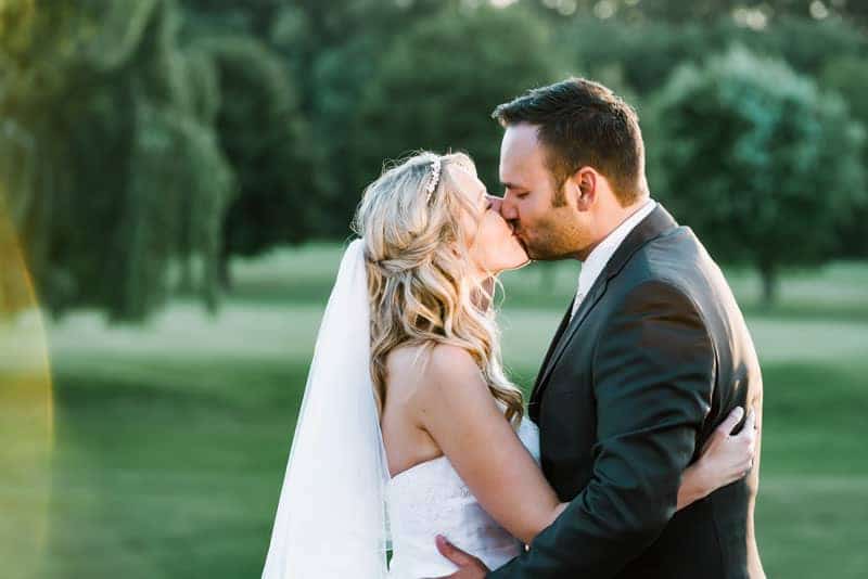 Eine Braut und ein Bräutigam küssen sich in der Sonne auf einem Golfplatz.