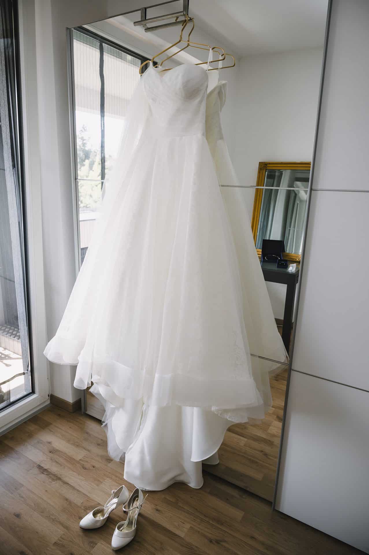 Vor einem Spiegel hängt ein Hochzeitskleid.