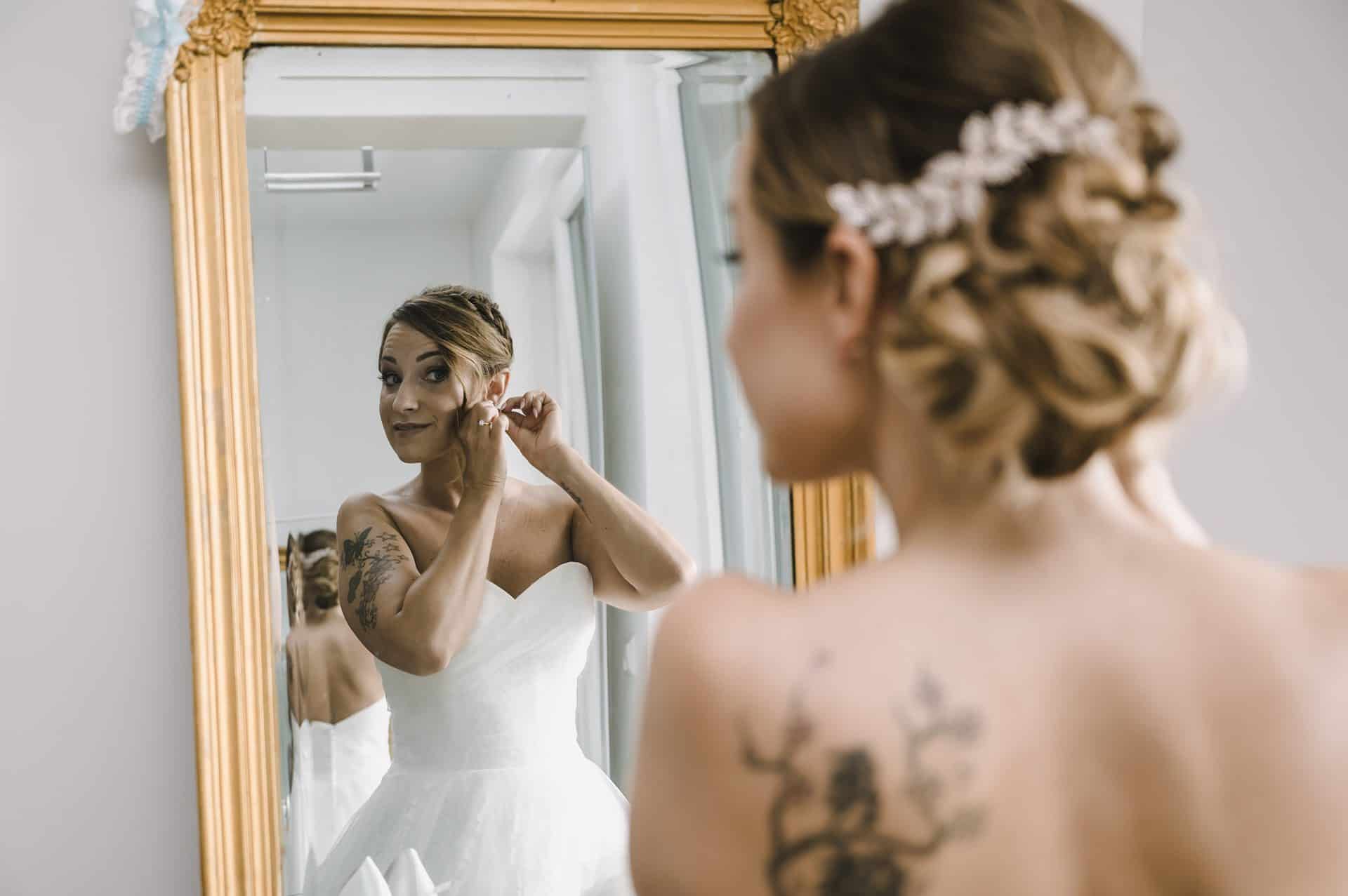 Eine Braut zieht ihr Hochzeitskleid vor einem Spiegel an.