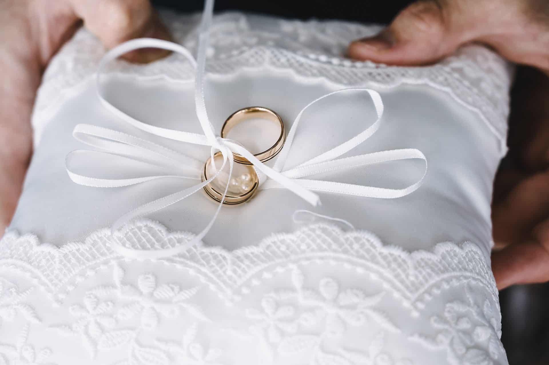 Eine Person hält einen Ehering auf einem weißen Kissen.