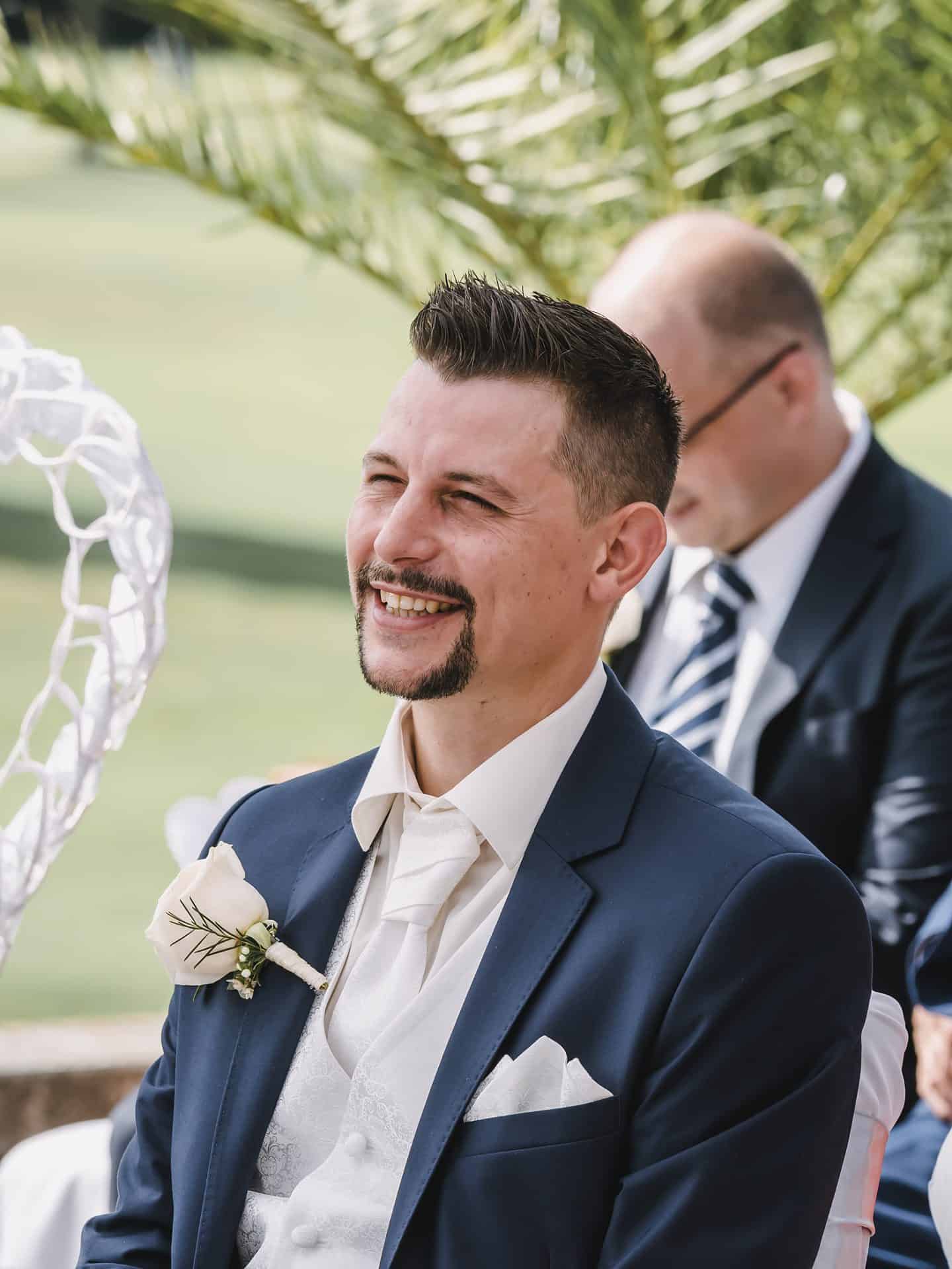 Ein Mann im Anzug lächelt bei einer Hochzeitszeremonie.
