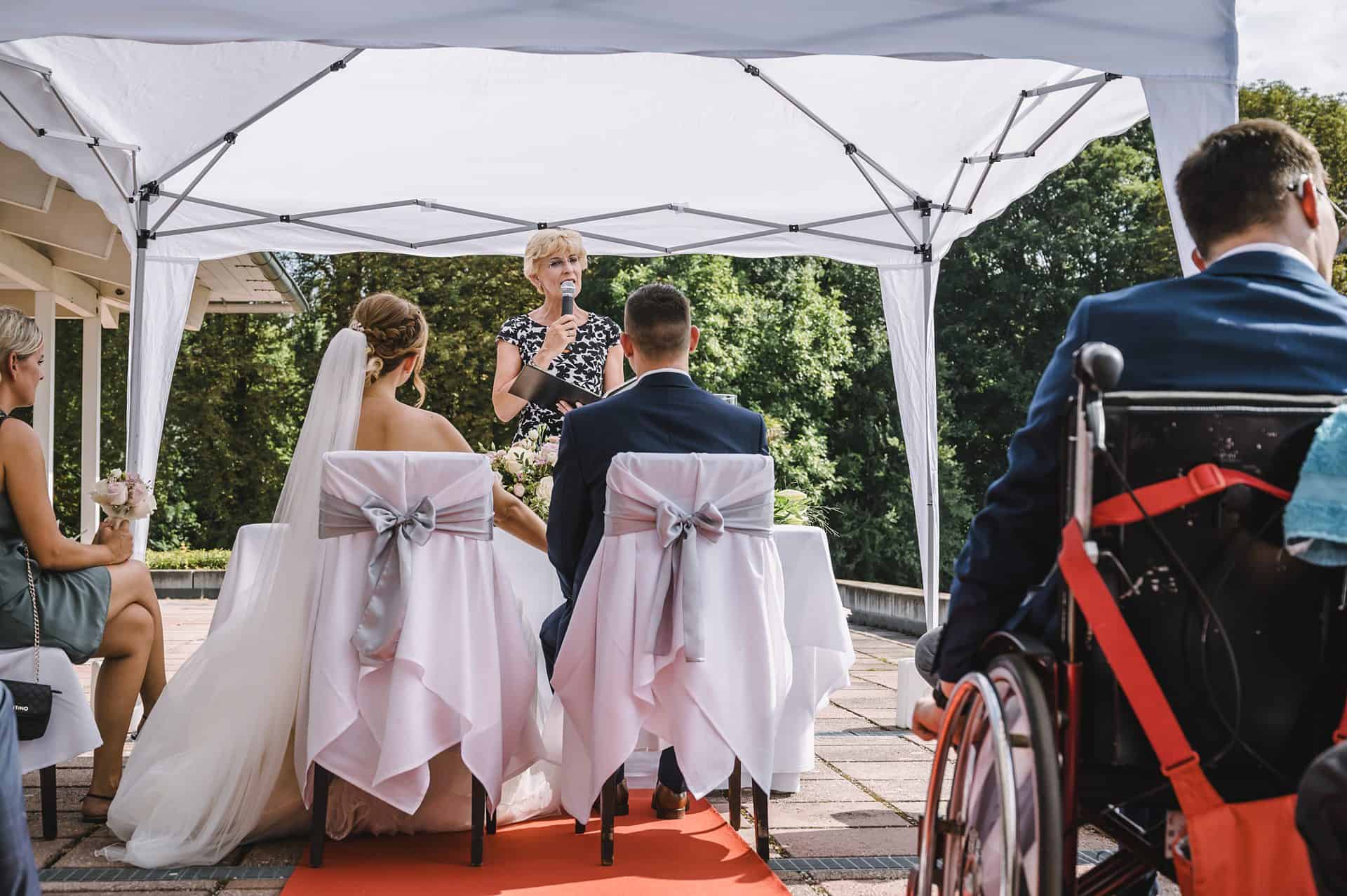 Eine Hochzeitszeremonie mit Menschen im Rollstuhl, die unter einem Zelt sitzen.
