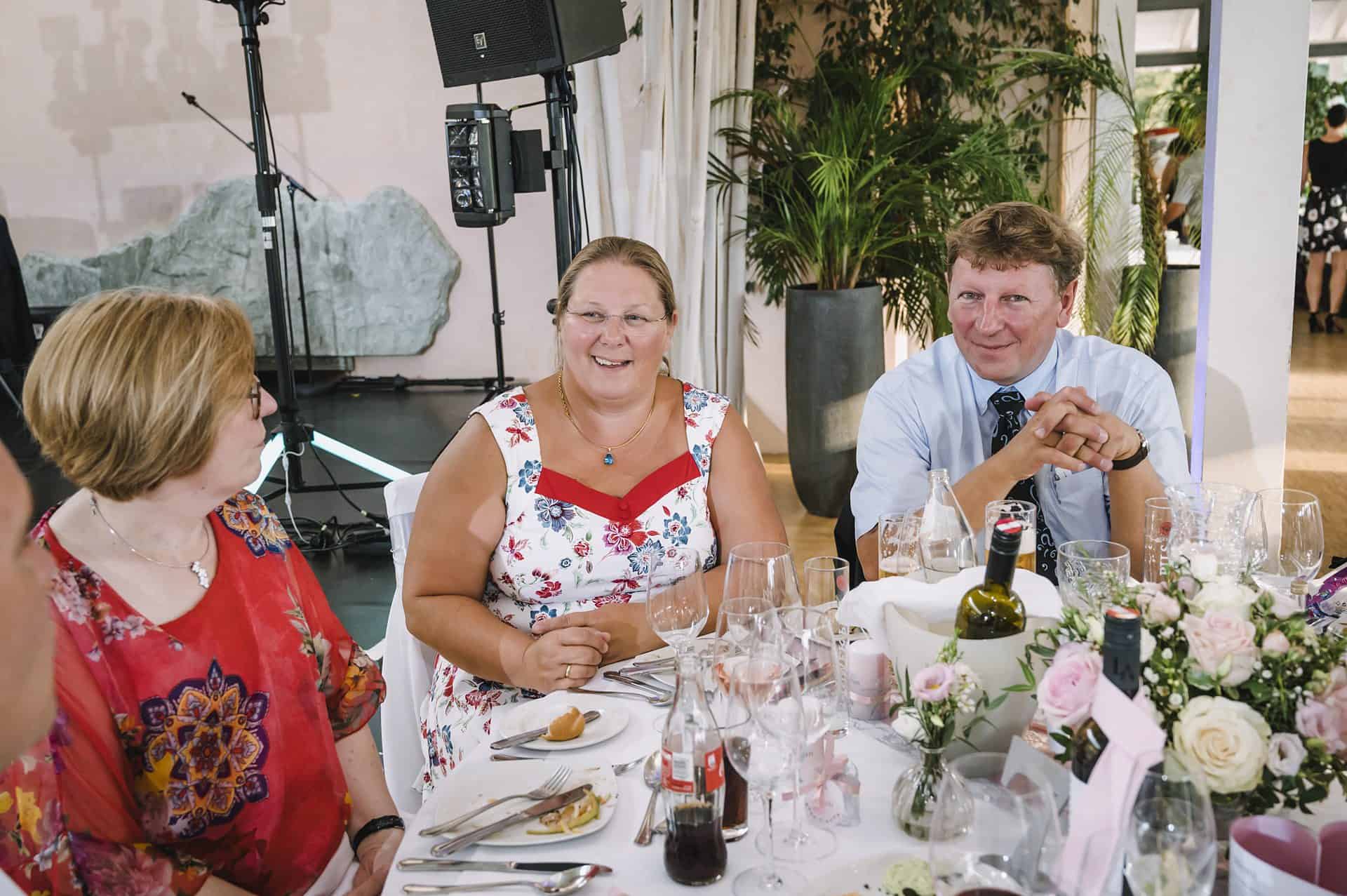 Eine Gruppe von Menschen sitzt bei einer Hochzeitsfeier um einen Tisch.