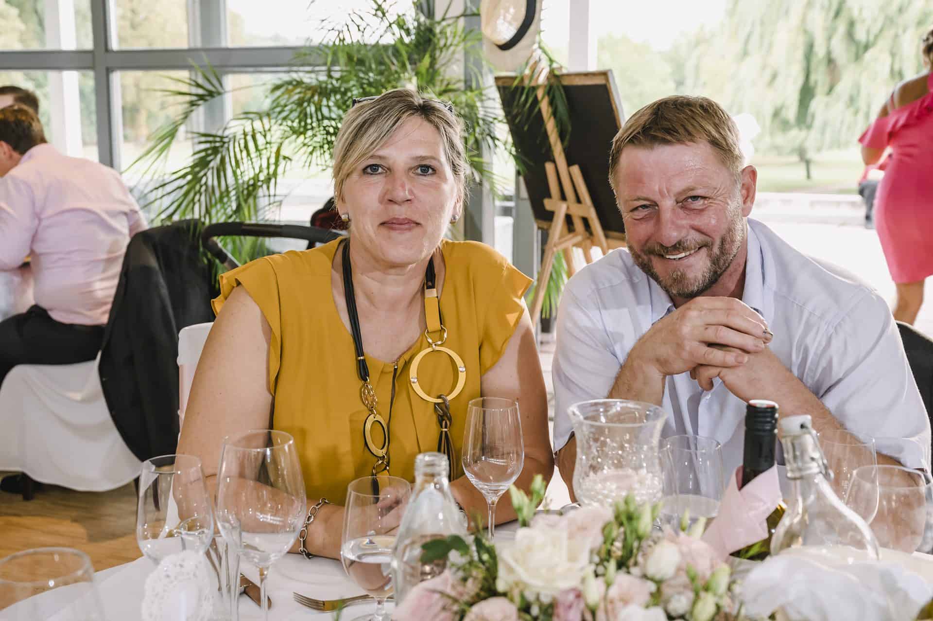 Ein Mann und eine Frau lächeln an einem Tisch bei einer Hochzeitsfeier.