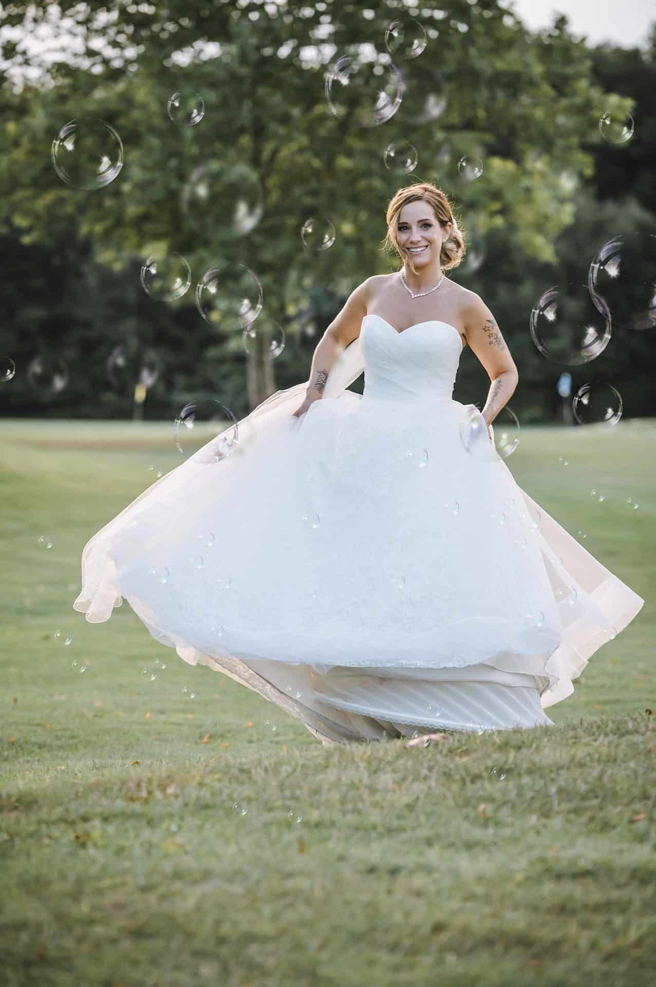 Eine Braut in einem Hochzeitskleid bläst Seifenblasen in ein Feld.