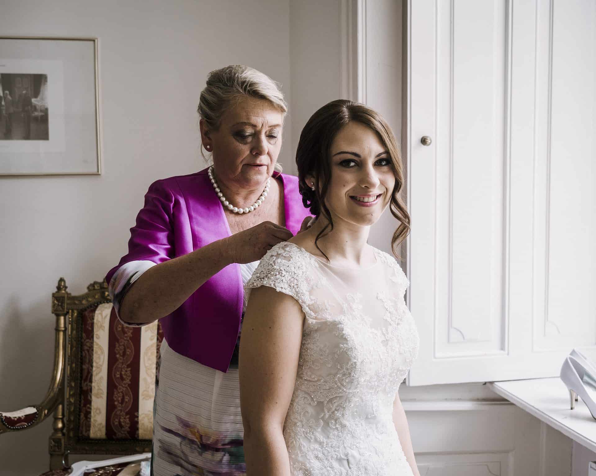 Eine Frau hilft ihrer Mutter, ihr Hochzeitskleid anzuziehen.