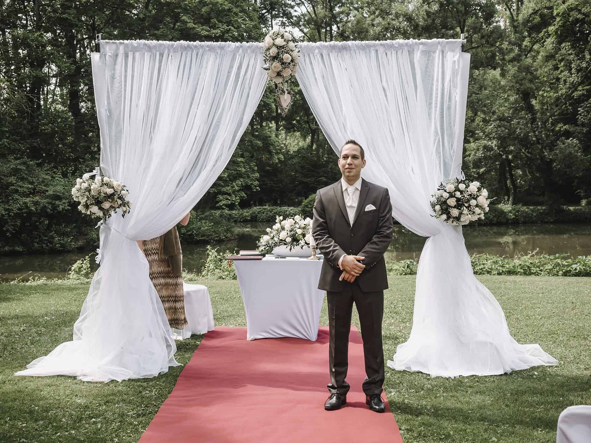 Ein Mann im Anzug steht vor einem Hochzeitsbogen.