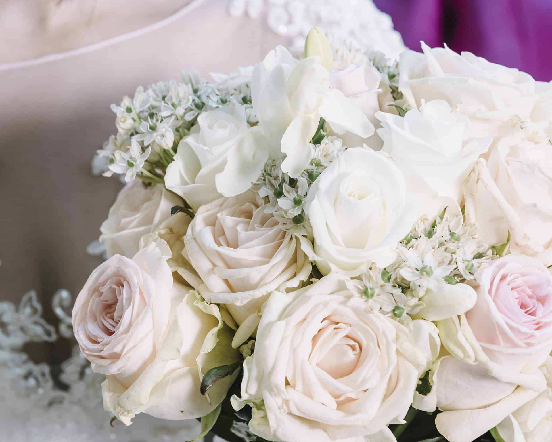 Eine Braut hält einen Strauß weißer und rosa Rosen in der Hand.