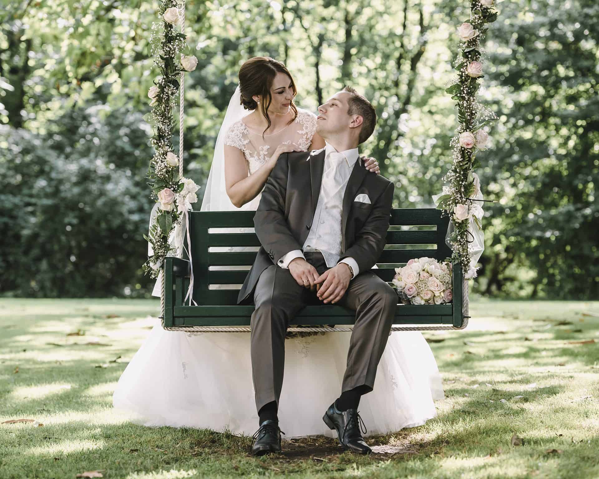 Eine Braut und ein Bräutigam sitzen auf einer Schaukel in einem Park.