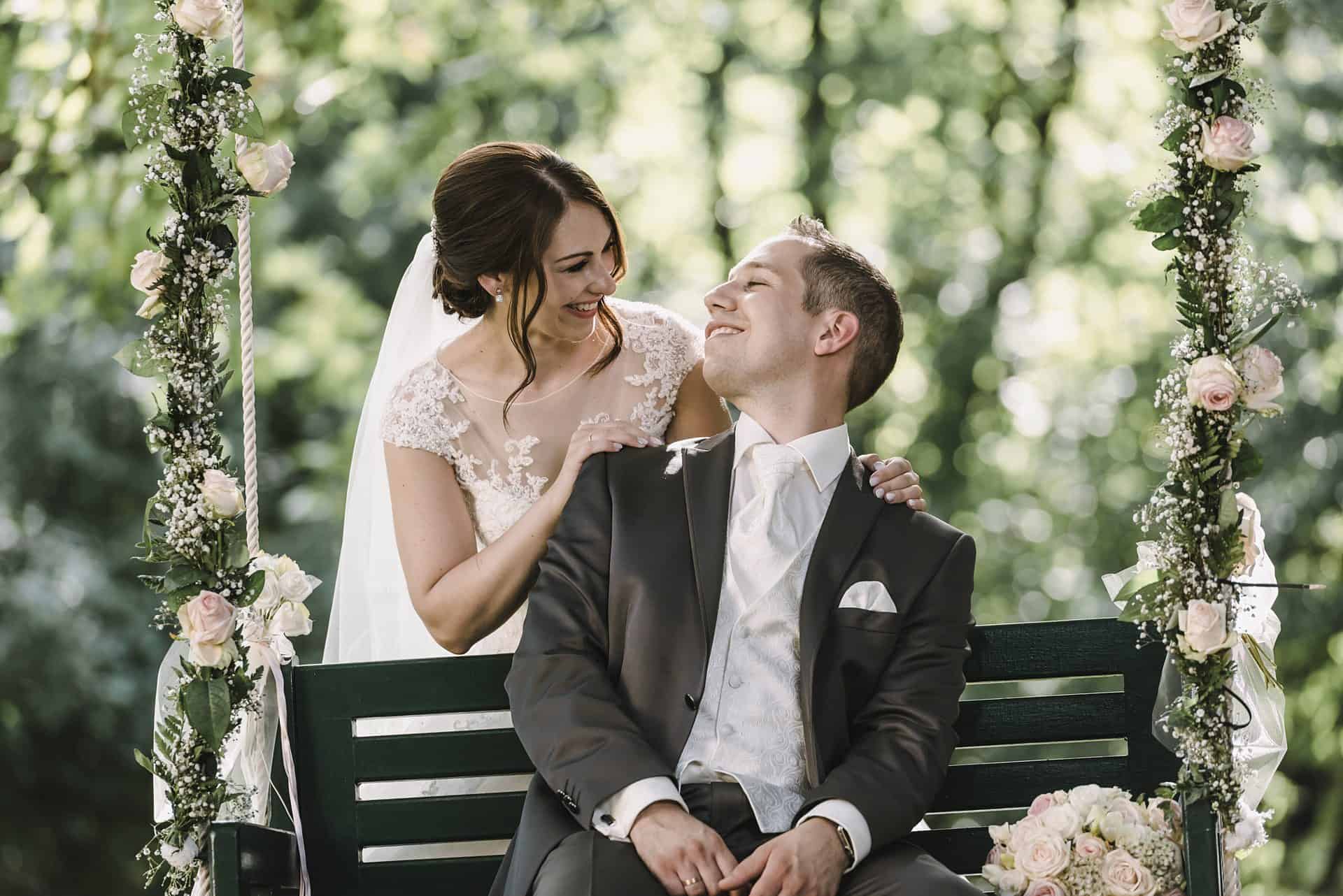 Eine Braut und ein Bräutigam sitzen auf einer Bank in einem Garten.