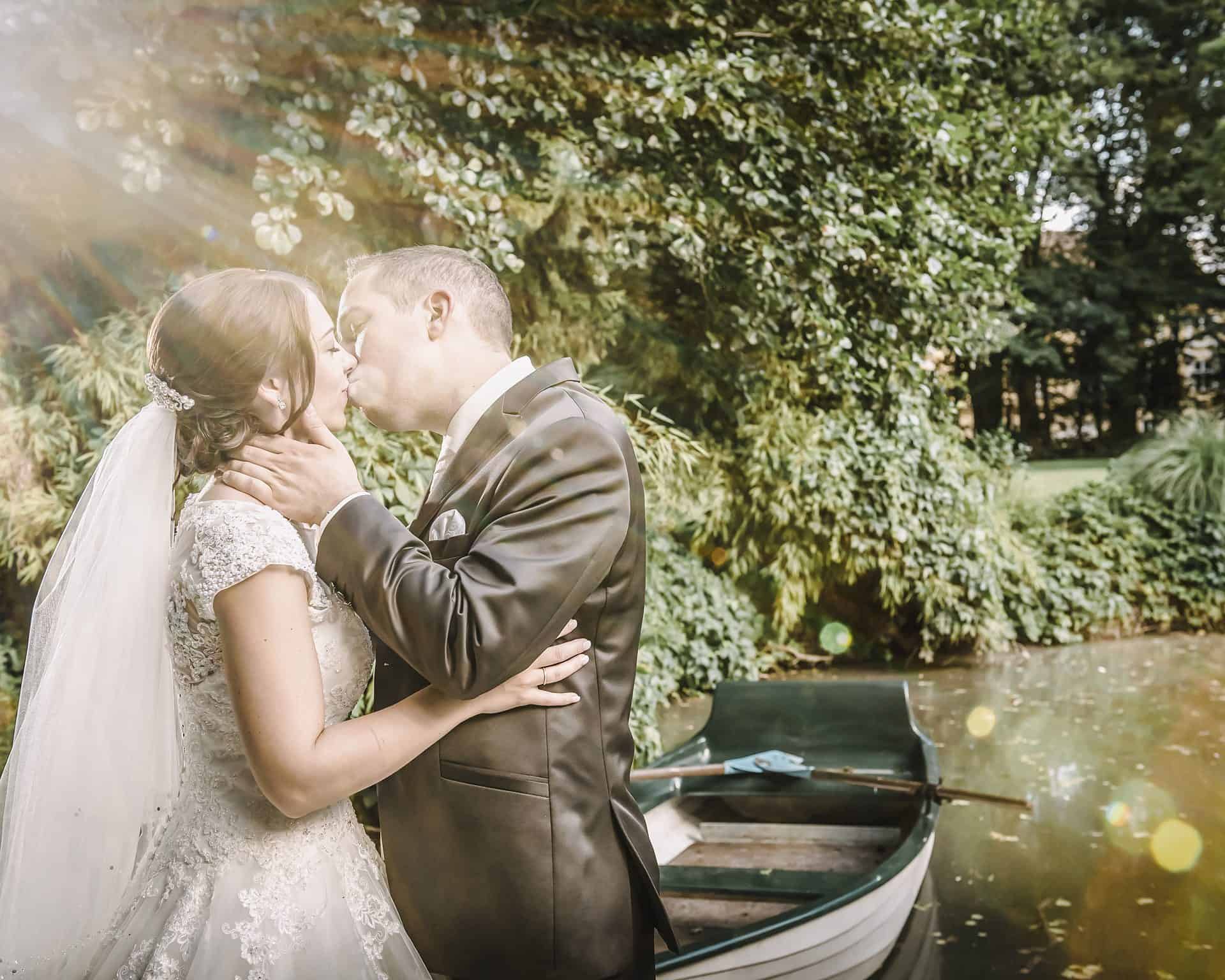 Eine Braut und ein Bräutigam küssen sich vor einem Boot in einem Teich.
