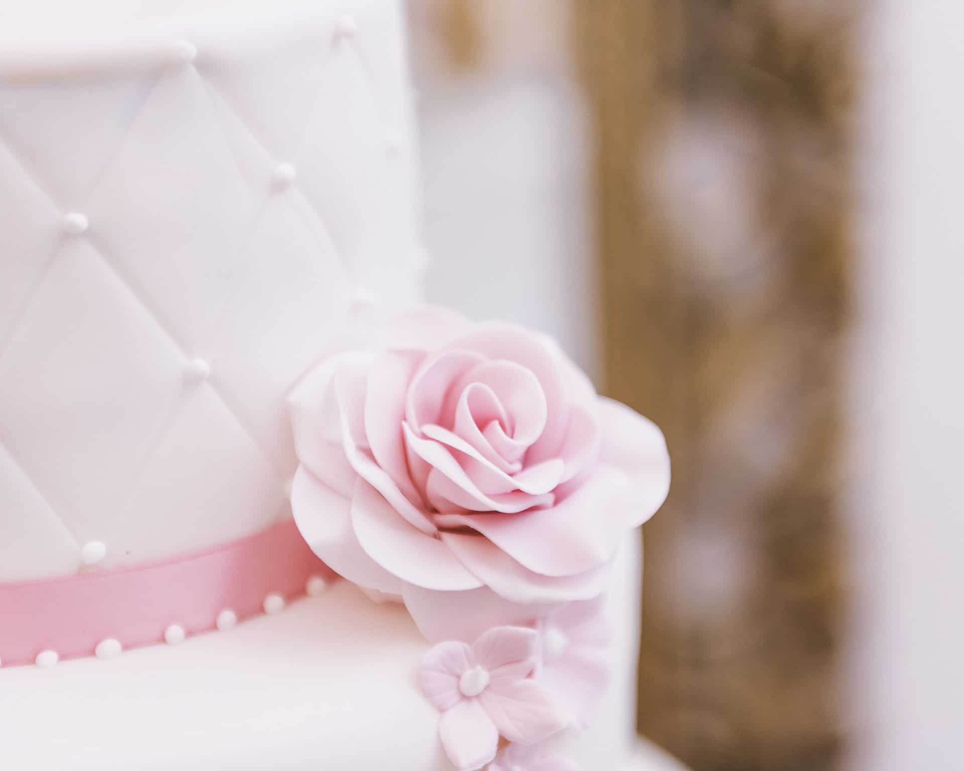 Eine weiße Hochzeitstorte mit einer rosa Blume oben drauf.